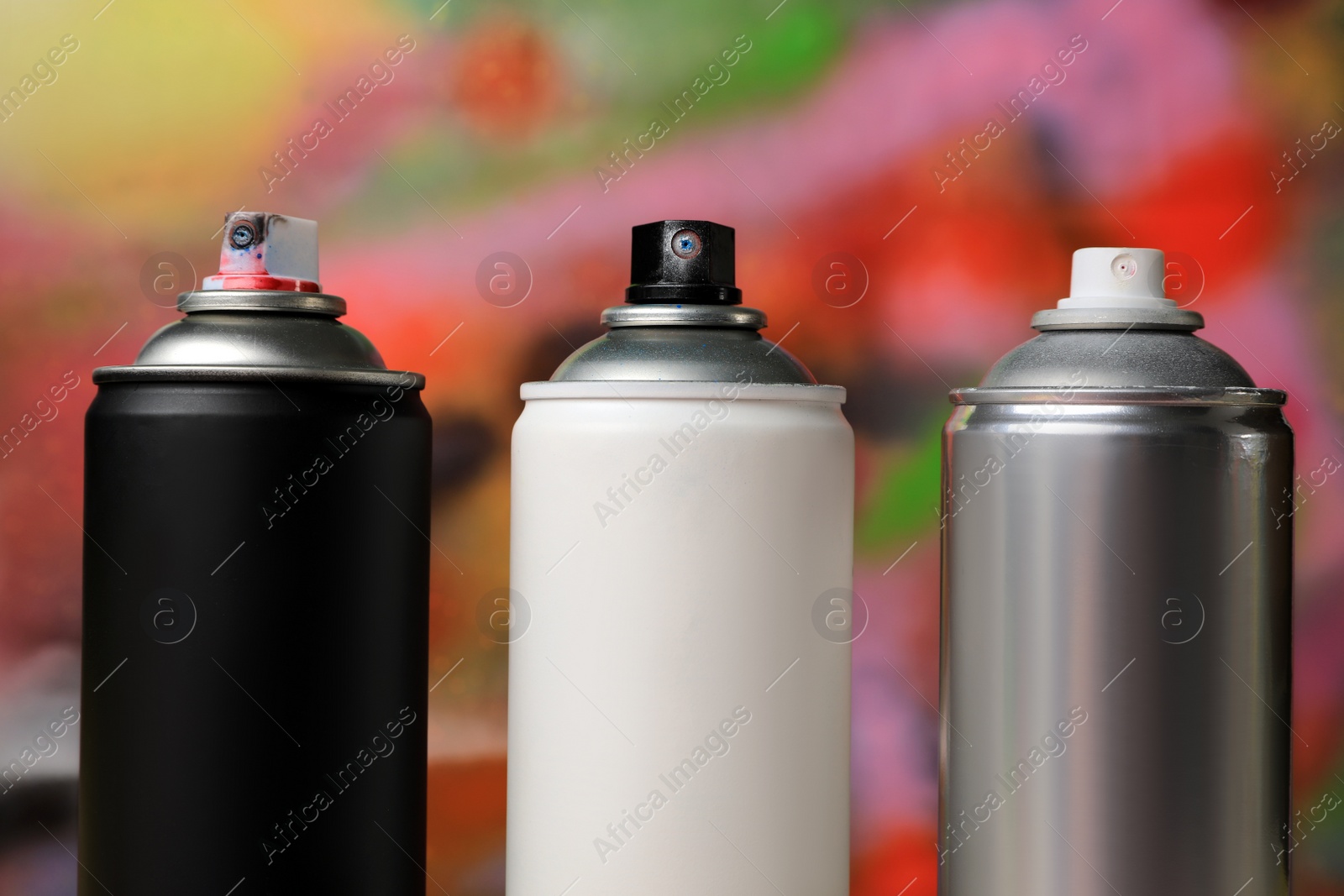 Photo of Cans of different graffiti spray paints on color background, closeup