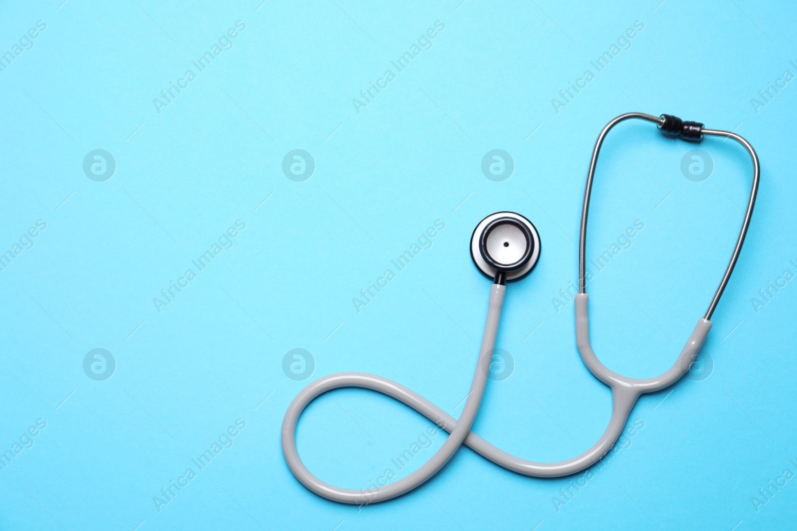 Photo of Stethoscope on light blue background, top view. Space for text