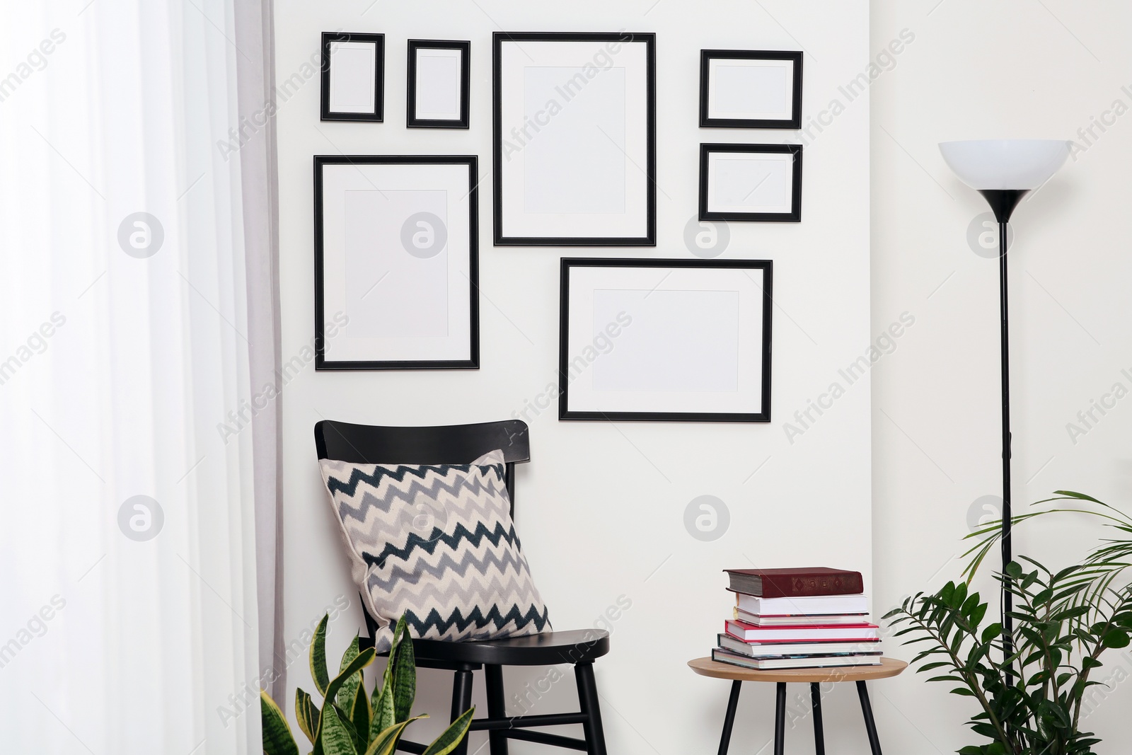 Photo of Empty frames hanging on white wall, wooden chair and table with books indoors