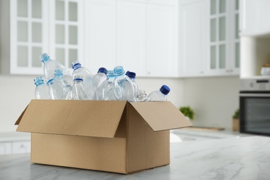 Photo of Cardboard box with used plastic bottles on table in kitchen, space for text. Recycling problem