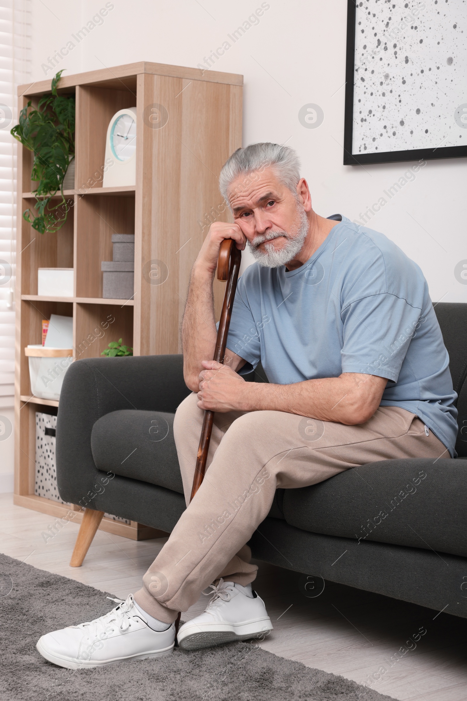 Photo of Senior man with walking cane sitting on sofa at home