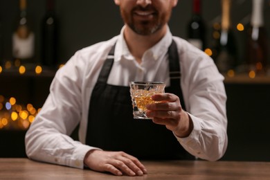 Bartender with glass of whiskey at bar counter indoors, closeup