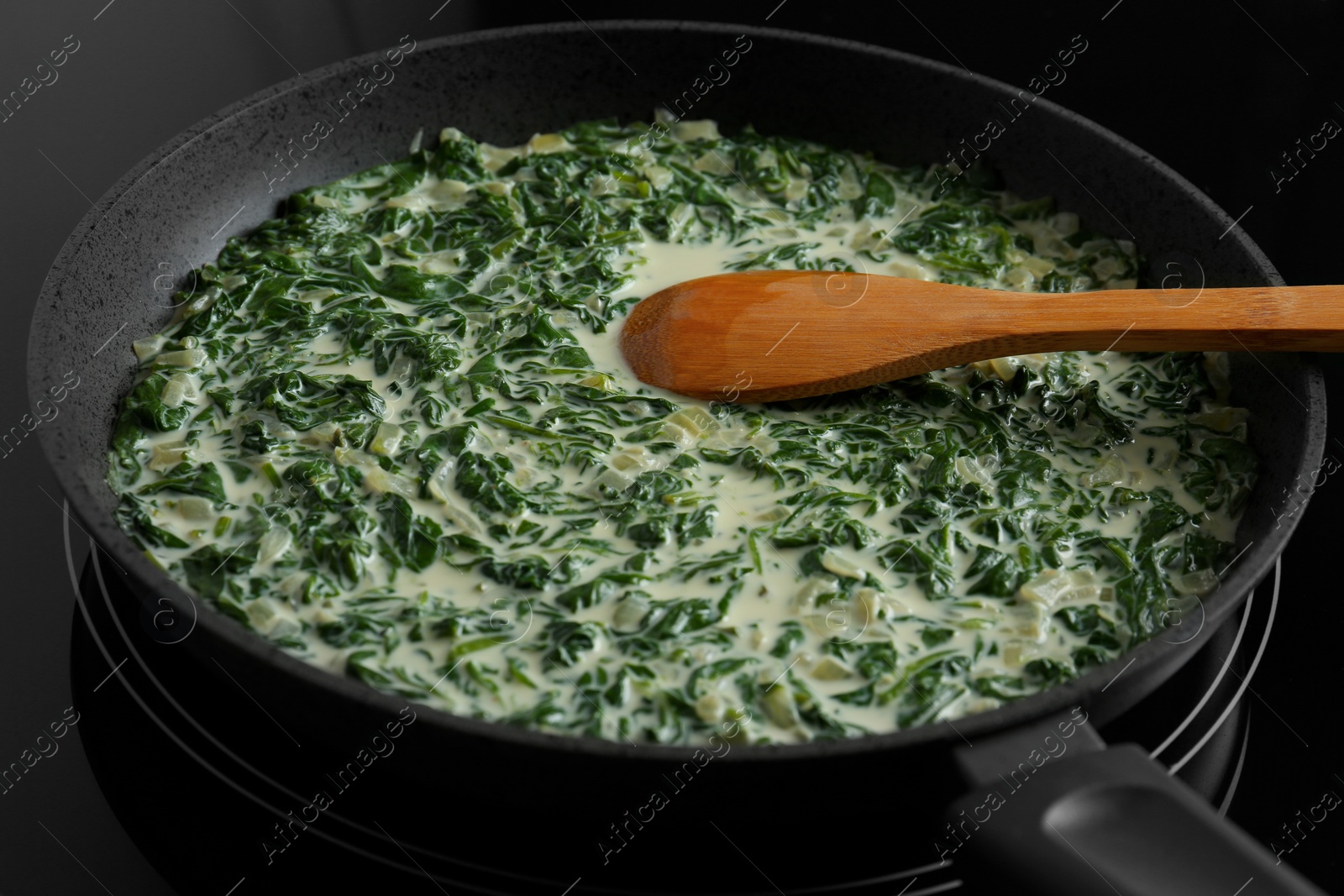 Photo of Tasty spinach dip with wooden spoon in frying pan on kitchen stove