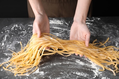 Photo of Woman holding raw egg noodles over grey table, closeup