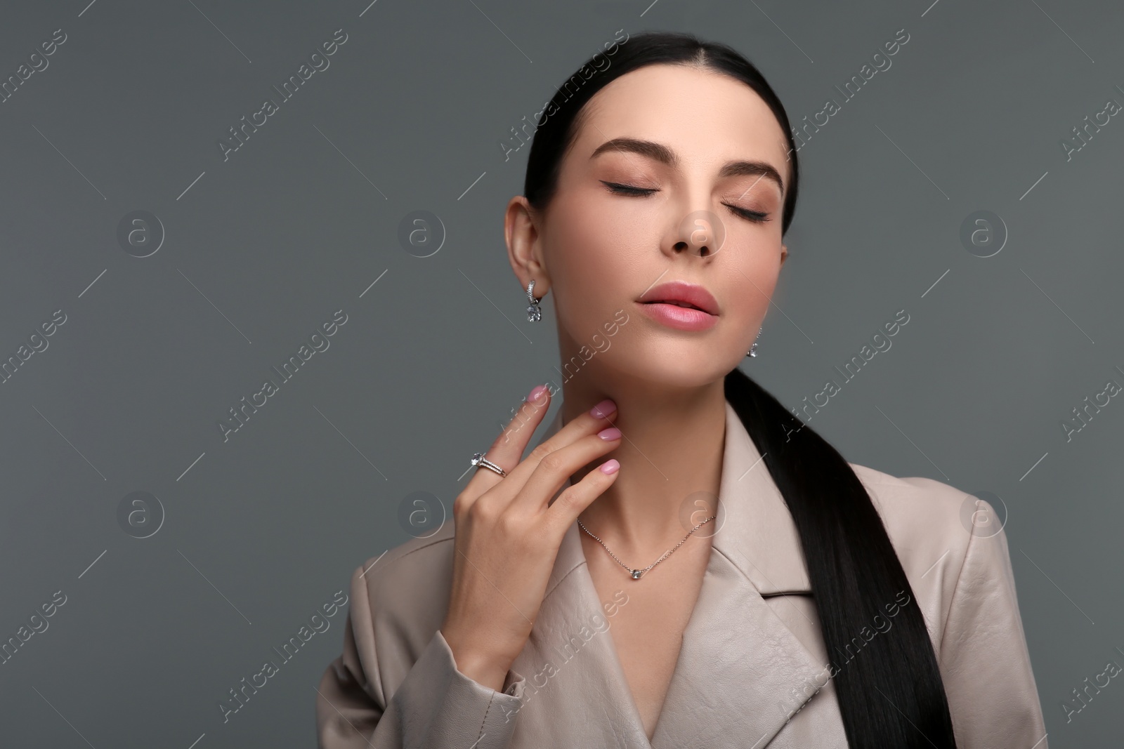 Photo of Beautiful young woman with elegant jewelry on dark grey background