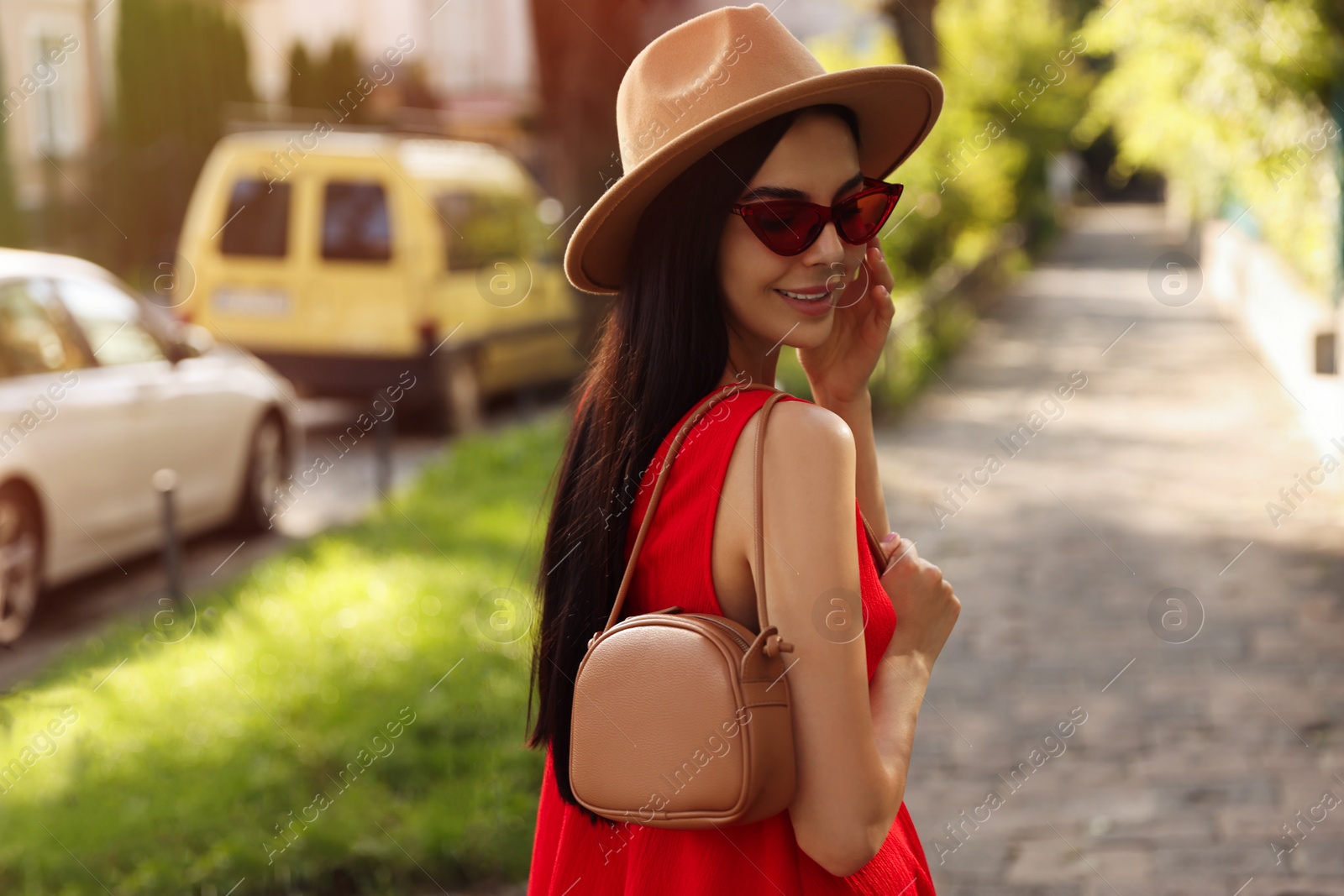 Photo of Beautiful young woman with stylish bag in red dress and sunglasses outdoors