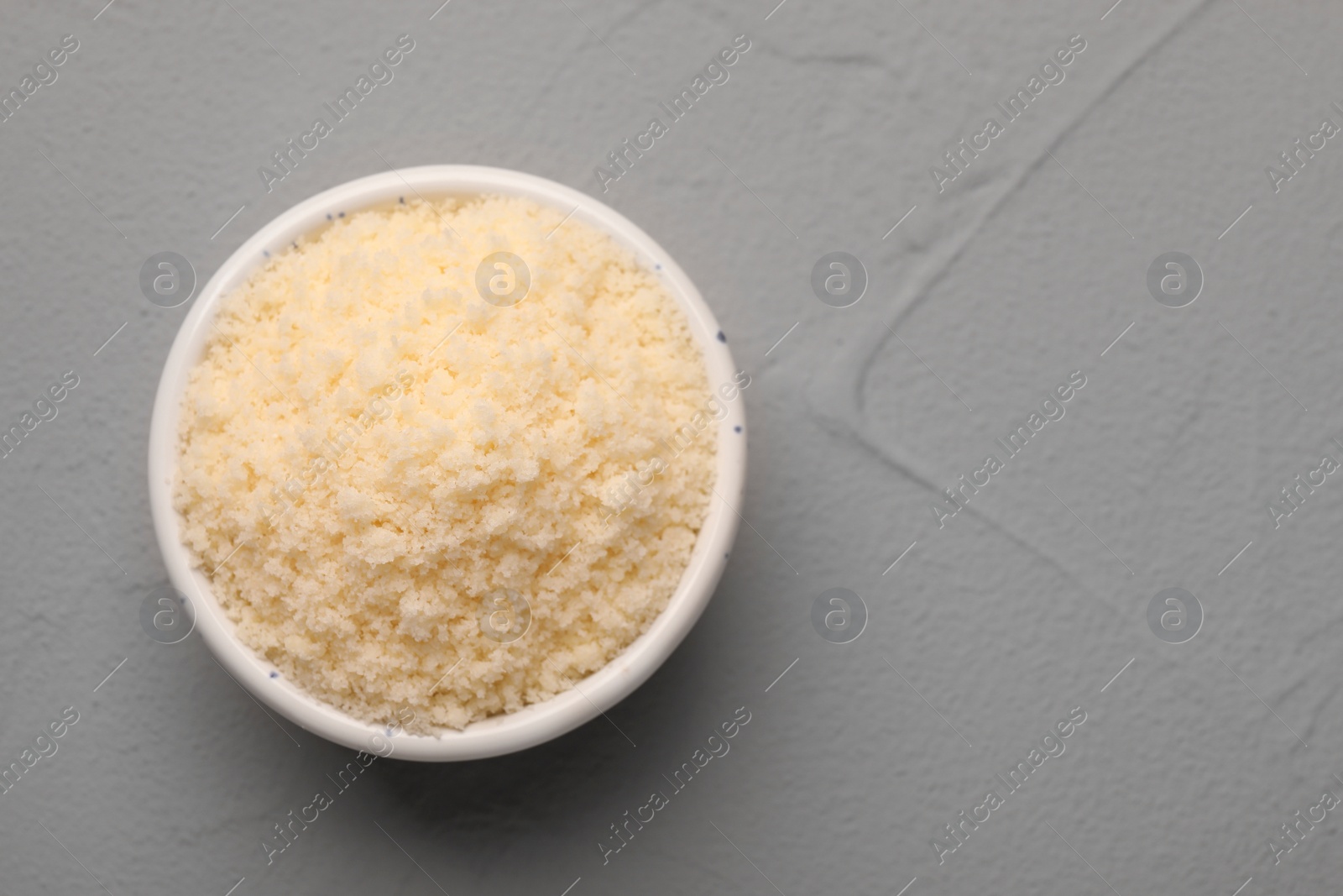 Photo of Delicious grated parmesan cheese in bowl on gray background. Space for text