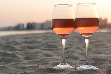 Photo of Glasses of tasty rose wine on sandy beach, space for text