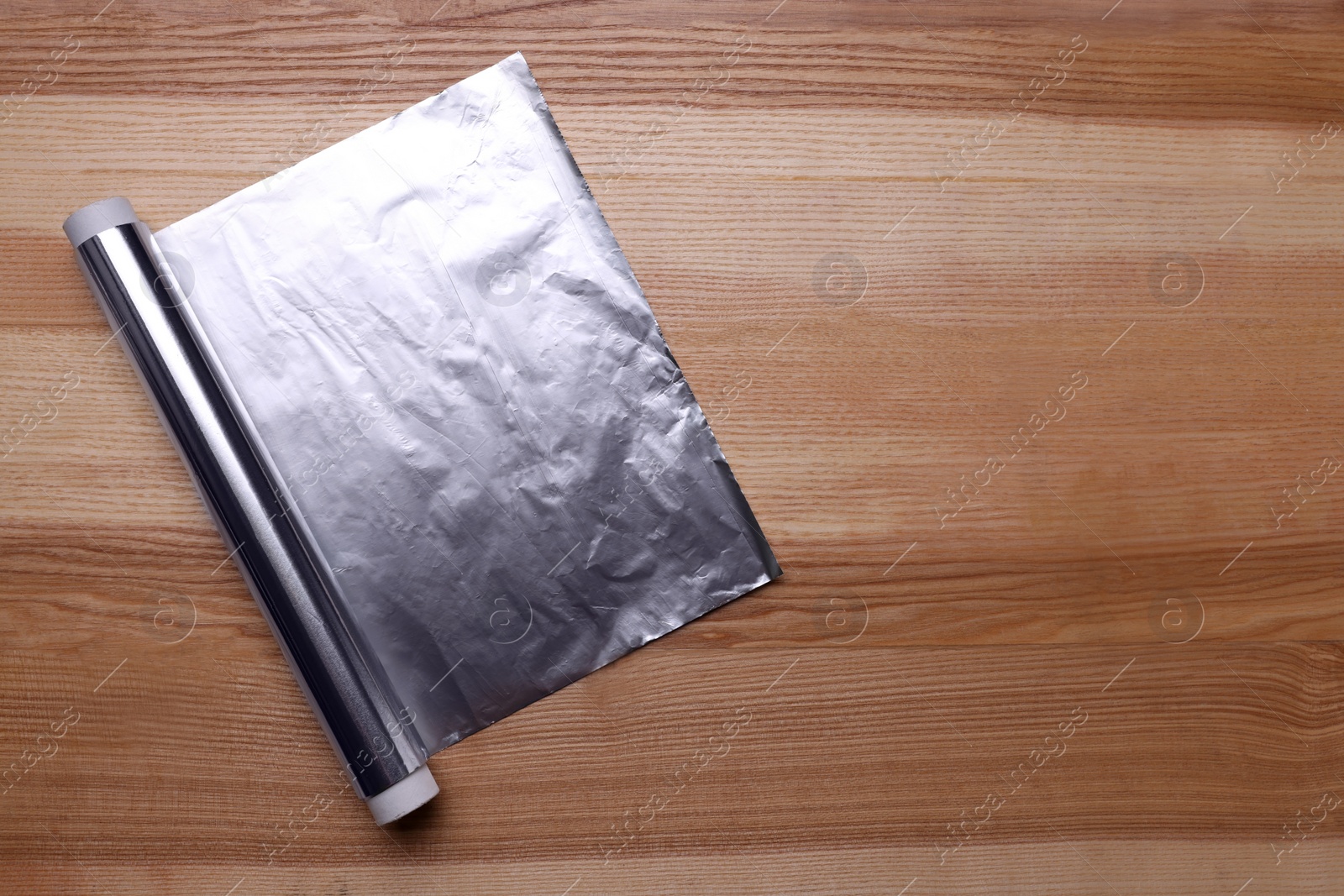 Photo of Roll of aluminum foil on wooden table, top view. Space for text