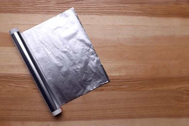 Photo of Roll of aluminum foil on wooden table, top view. Space for text