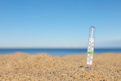 Weather thermometer in sand near sea, space for text