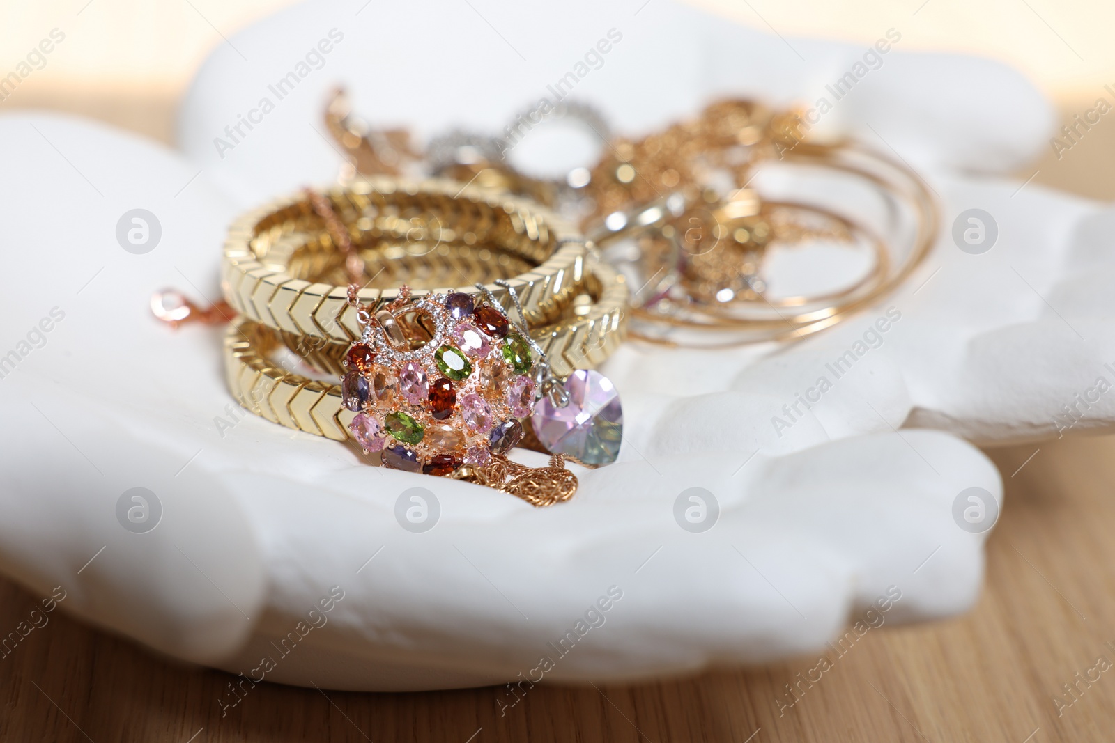 Photo of Ceramic hand stand with stylish bracelets and other accessories on wooden table, closeup