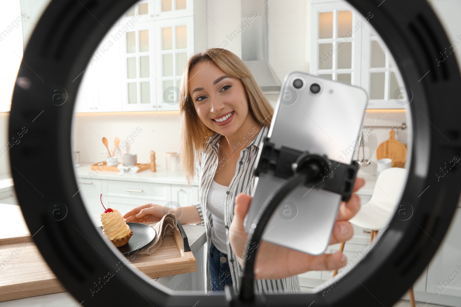 Photo of Blogger preparing for video recording in kitchen at home. Using smartphone and ring lamp