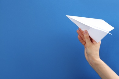 Woman holding paper plane on blue background, closeup. Space for text