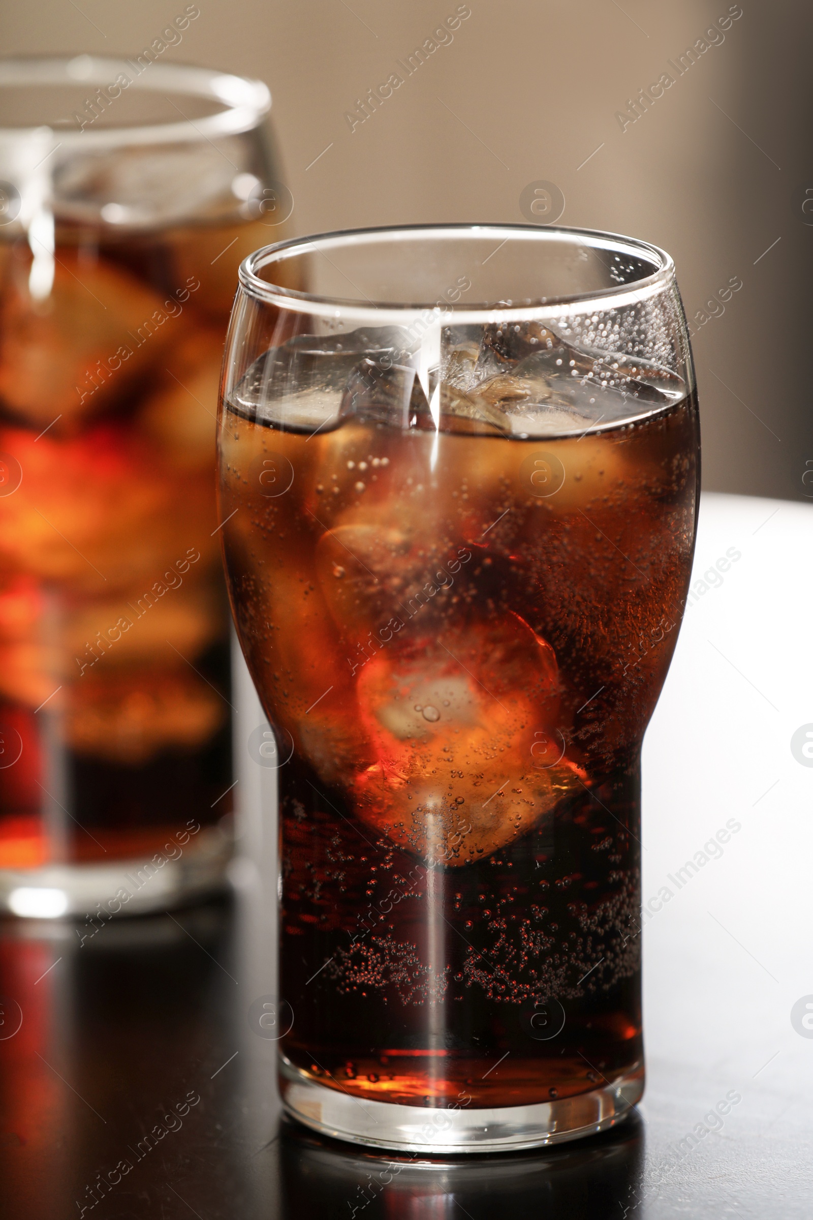 Photo of Glass of cola with ice on table against blurred background