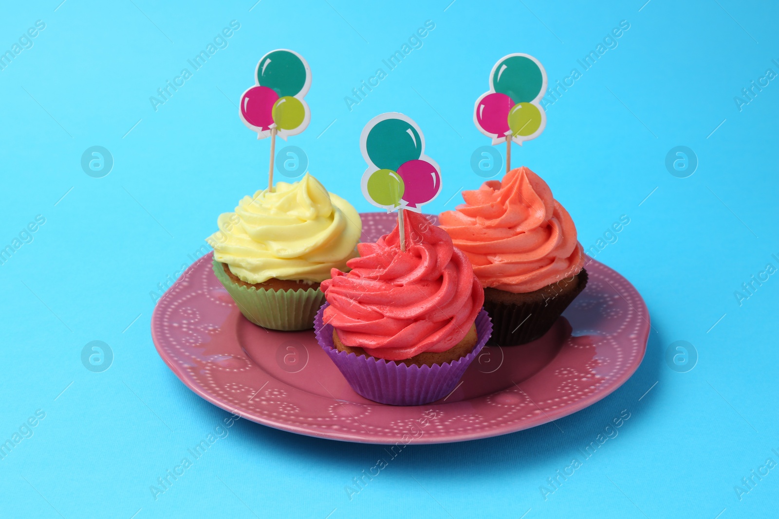 Photo of Delicious cupcakes with bright cream and toppers on light blue background