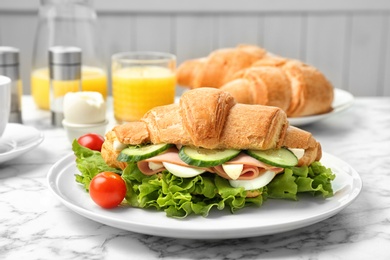 Tasty croissant sandwich with sausage on table