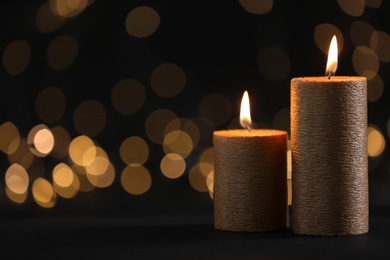 Photo of Burning gold candles against blurred lights in darkness. Space for text