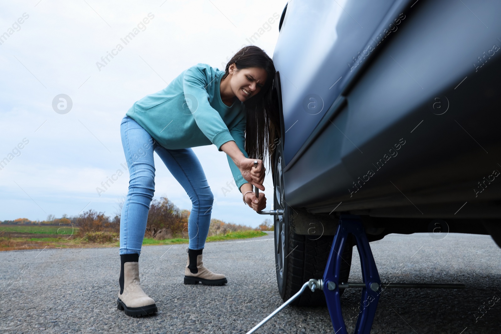 Photo of Young woman changing tire of car outdoors