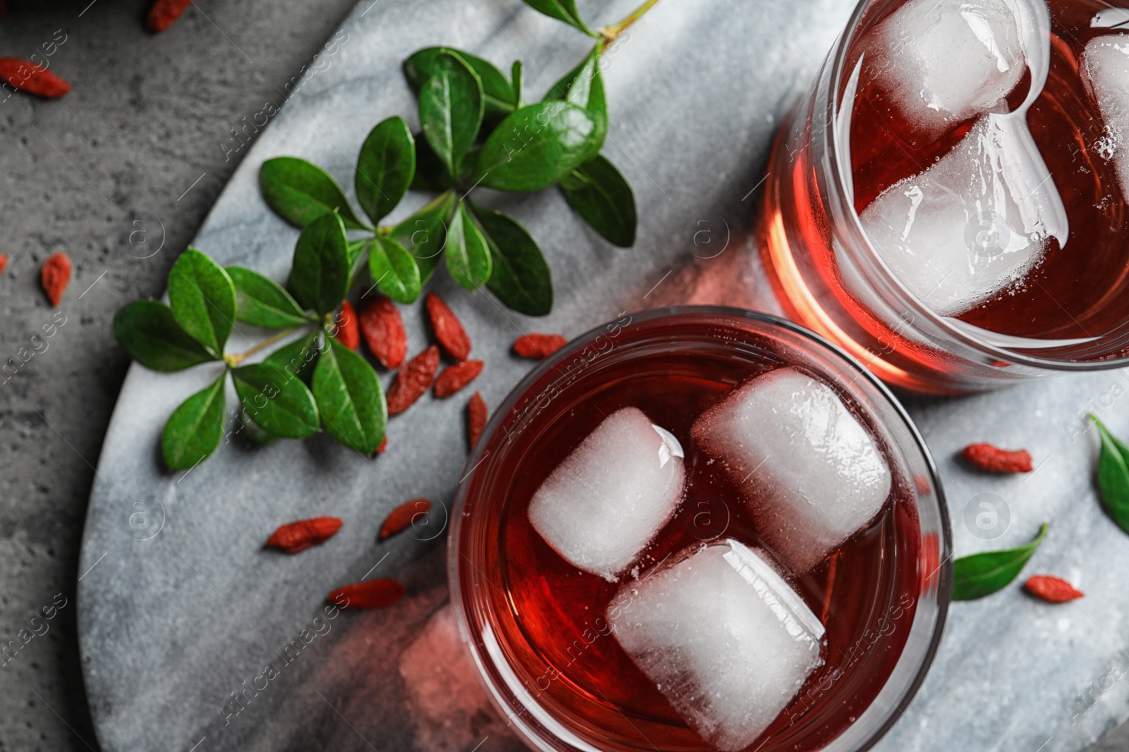 Photo of Healthy goji juice in glasses served on grey table, flat lay