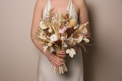 Bride holding beautiful dried flower bouquet on beige background, closeup