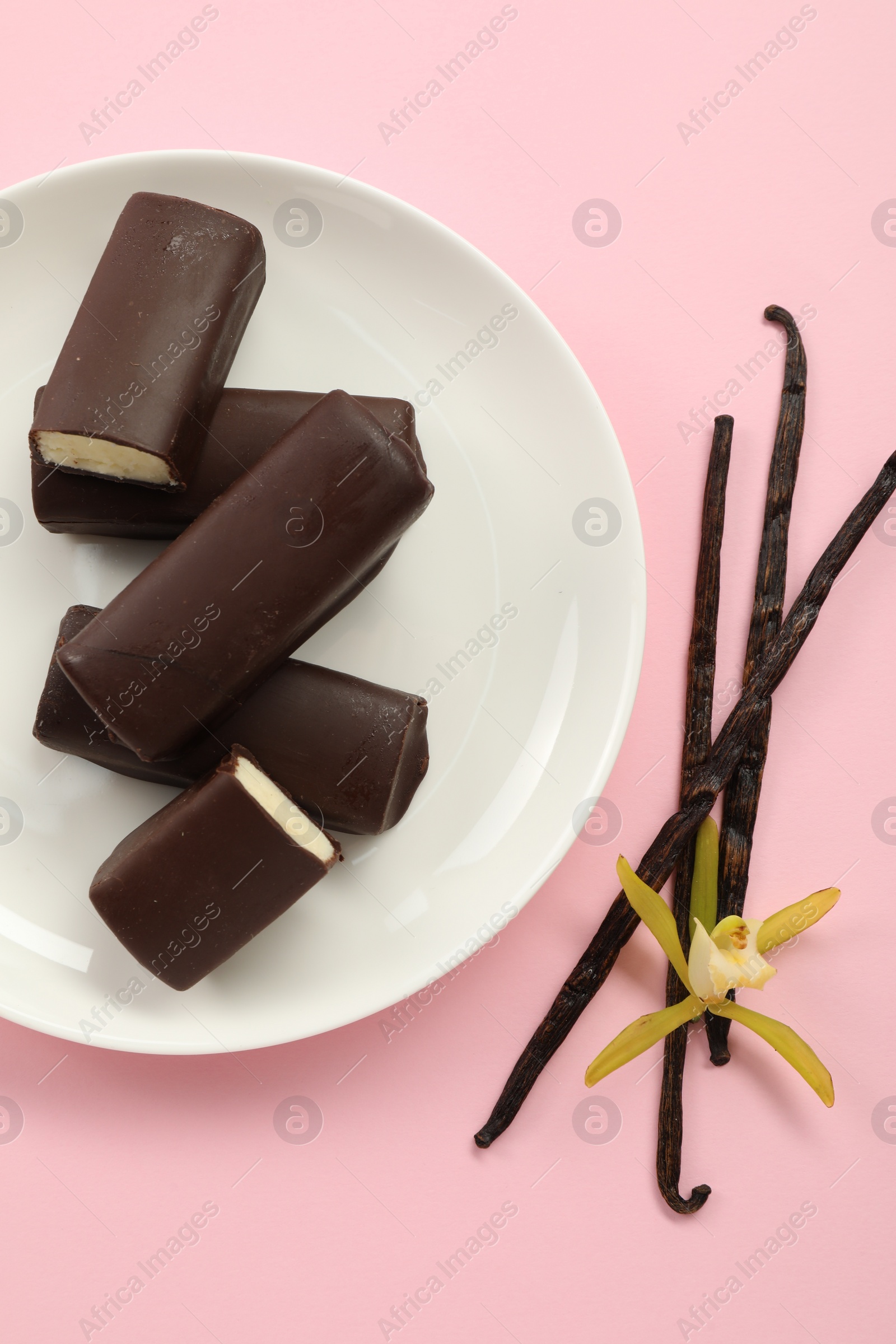 Photo of Glazed curd cheese bars, vanilla pods and flower on pink background, top view