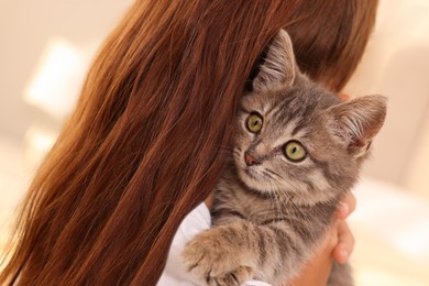 Photo of Cute little girl with kitten indoors, back view. Childhood pet