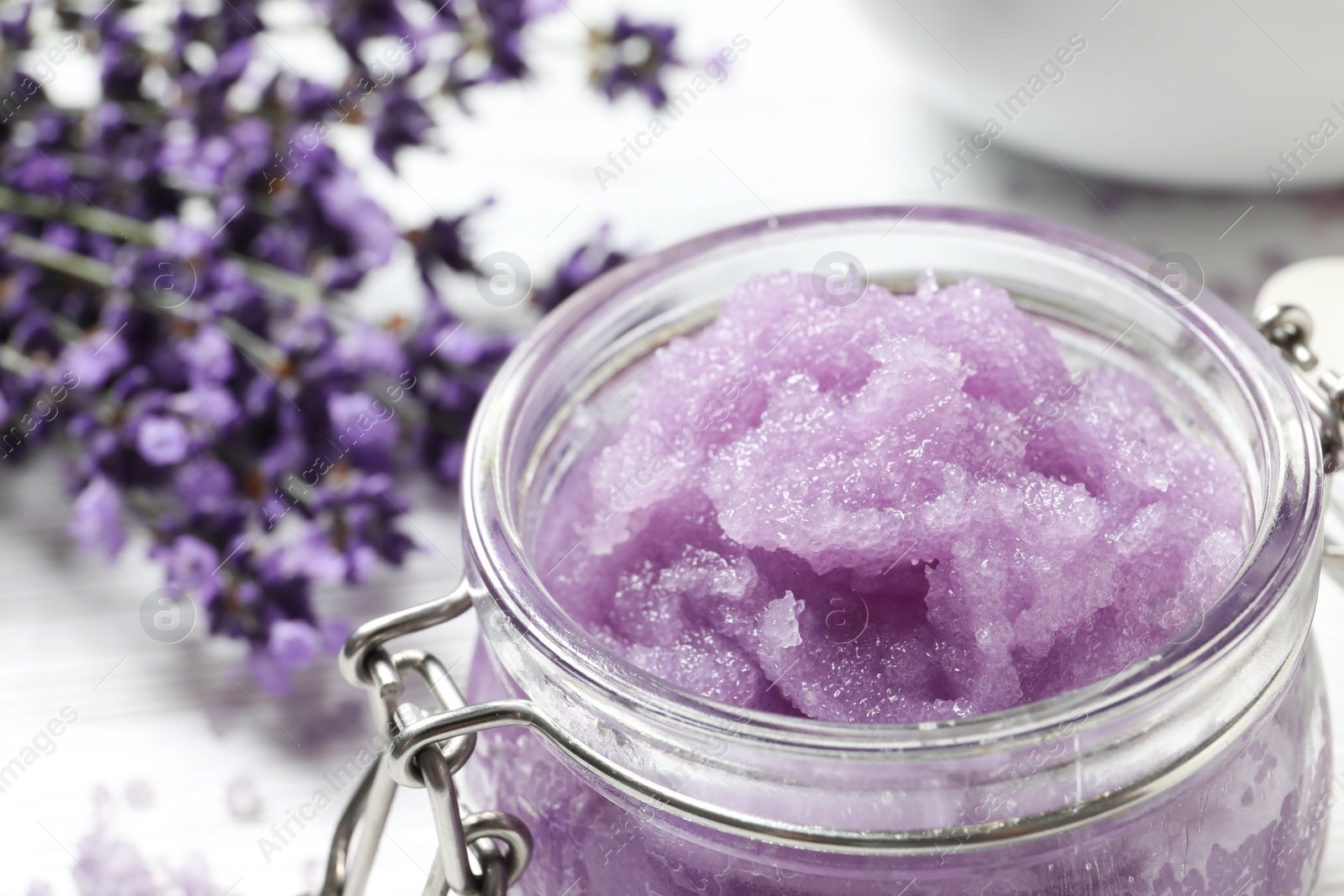 Photo of Glass jar of natural sugar scrub and lavender flowers on table, closeup with space for text. Cosmetic product