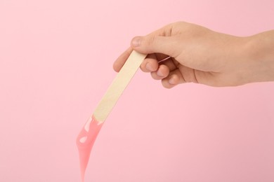Woman holding spatula with hot depilatory wax on pink background, closeup