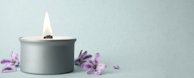 Photo of Beautiful candle with wooden wick and flowers on light background, space for text