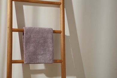 Photo of Violet towel hanging on wooden ladder indoors. Space for text