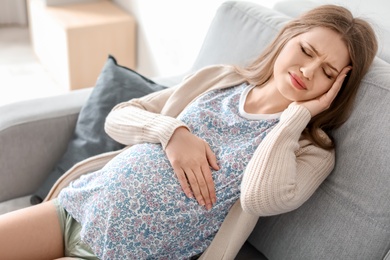 Photo of Young pregnant woman suffering from headache at home