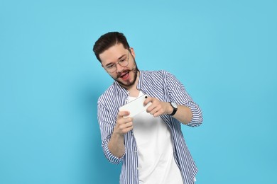 Emotional man playing game on phone against light blue background