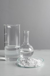 Photo of Petri dish with calcium carbonate powder and laboratory glassware on white table
