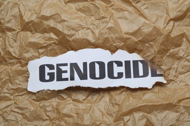 Photo of Piece of burnt card with word Genocide on crumpled paper, top view