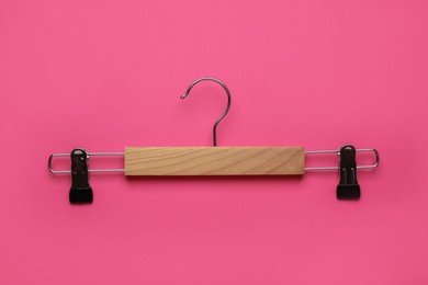 Photo of Empty wooden hanger with clips on pink background, top view