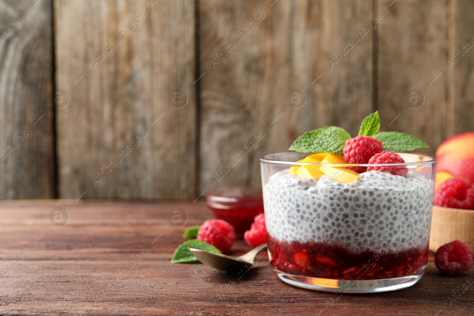 Photo of Delicious chia pudding with raspberries, peach and mint on wooden table, space for text