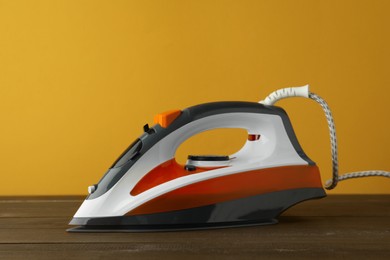 Photo of One modern iron on wooden table against orange background. Home appliance