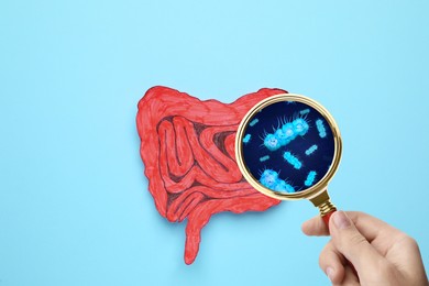 Image of Microorganisms research. Woman with magnifying glass and paper intestine cutout on light blue, top view