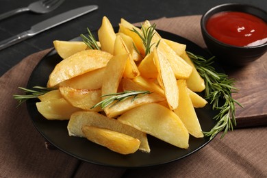 Plate with tasty baked potato wedges, rosemary and sauce on table, closeup
