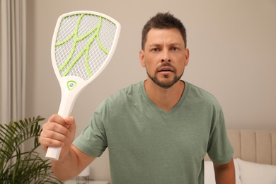 Man with electric fly swatter in bedroom. Insect killer