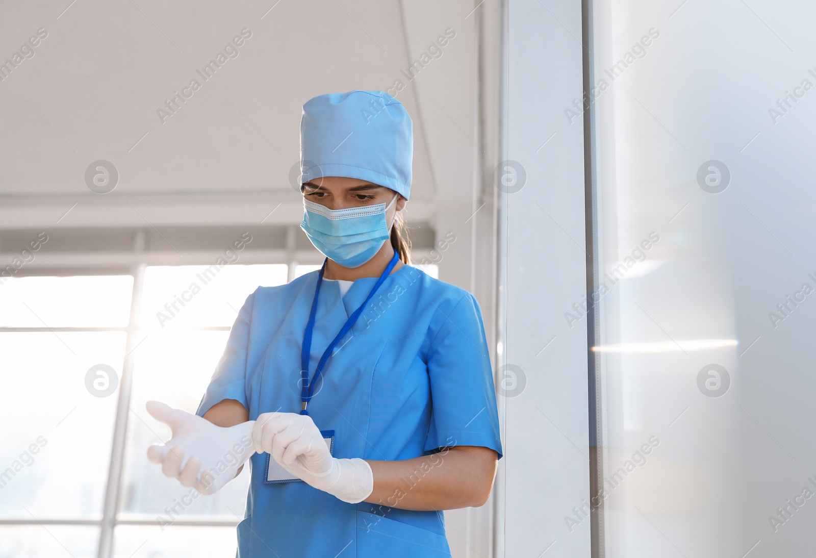 Photo of Doctor in protective mask and scrubs putting on medical gloves indoors. Space for text