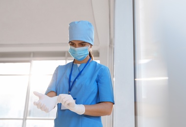 Photo of Doctor in protective mask and scrubs putting on medical gloves indoors. Space for text