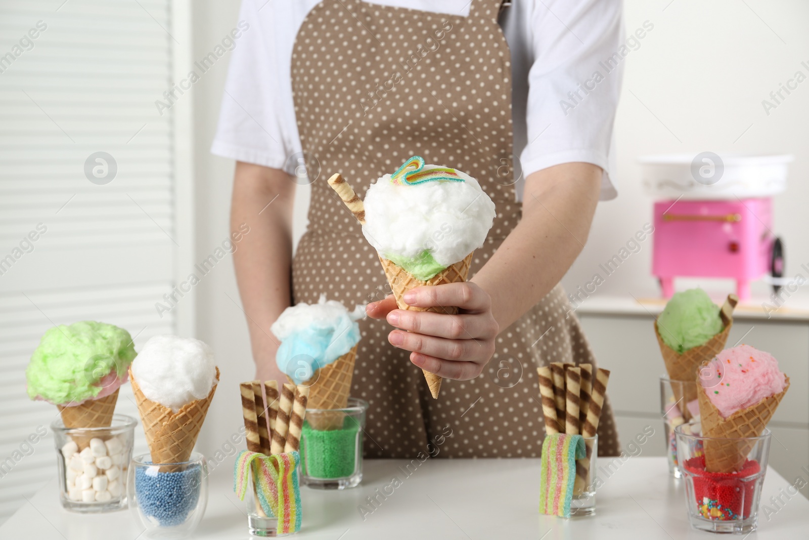 Photo of Woman holding waffle cone with cotton candy indoors, closeup