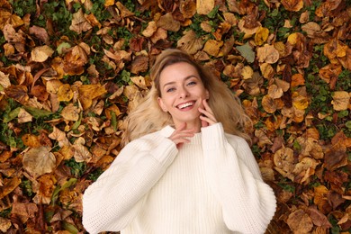 Smiling woman lying among autumn leaves outdoors, top view