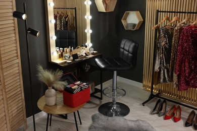 Photo of Makeup room. Stylish mirror near dressing table with beauty products, chair and clothes rack indoors