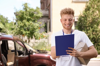 Photo of Young delivery courier with parcel and clipboard outdoors. Space for text