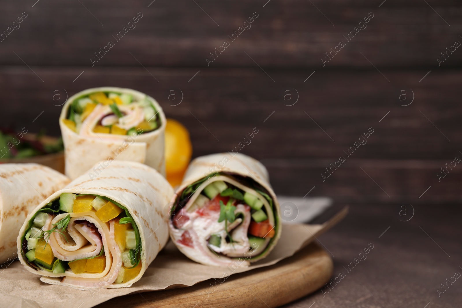 Photo of Delicious sandwich wraps with fresh vegetables on grey table, closeup. Space for text