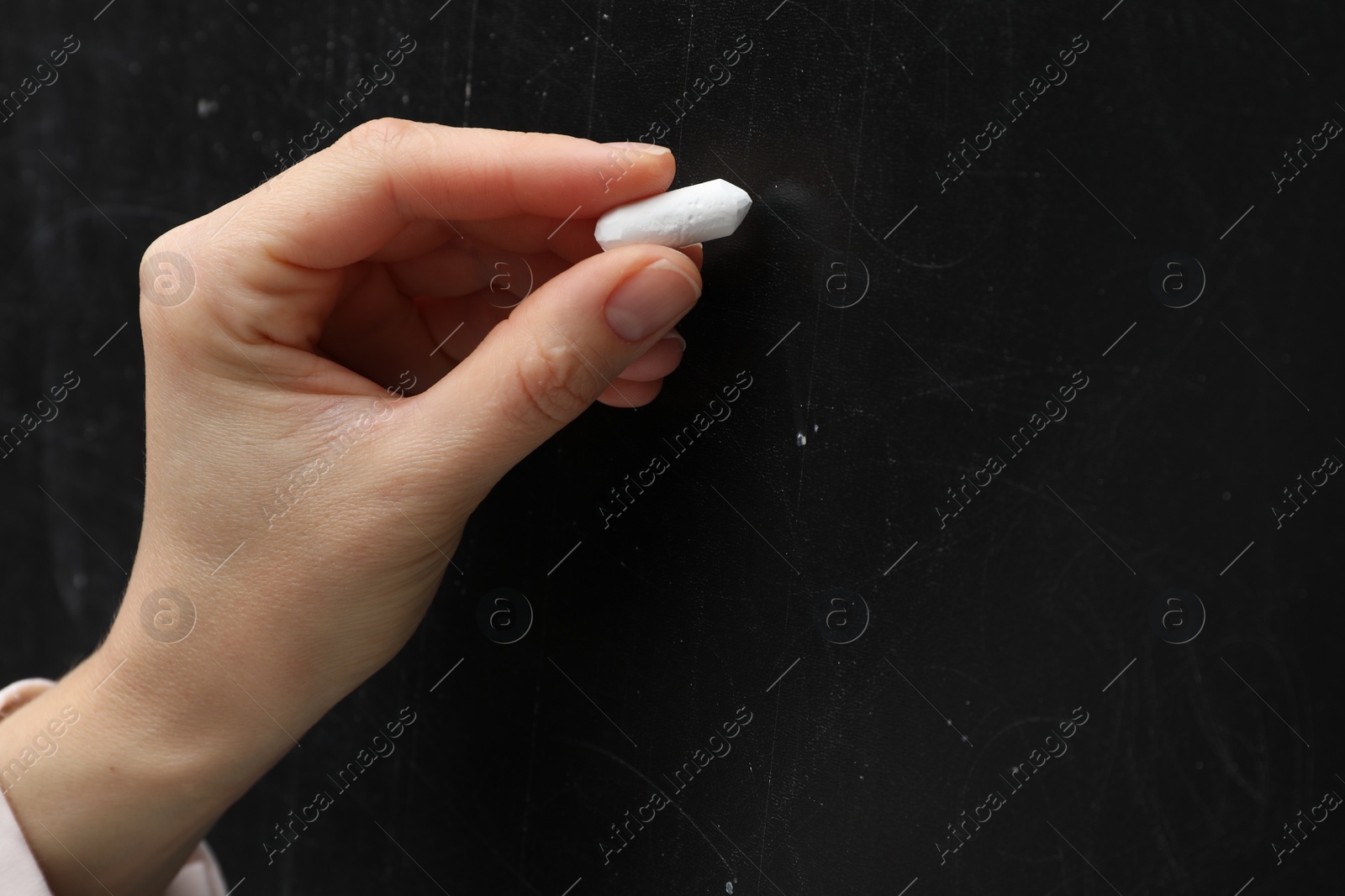 Photo of Teacher writing with chalk on black chalkboard, closeup. Space for text