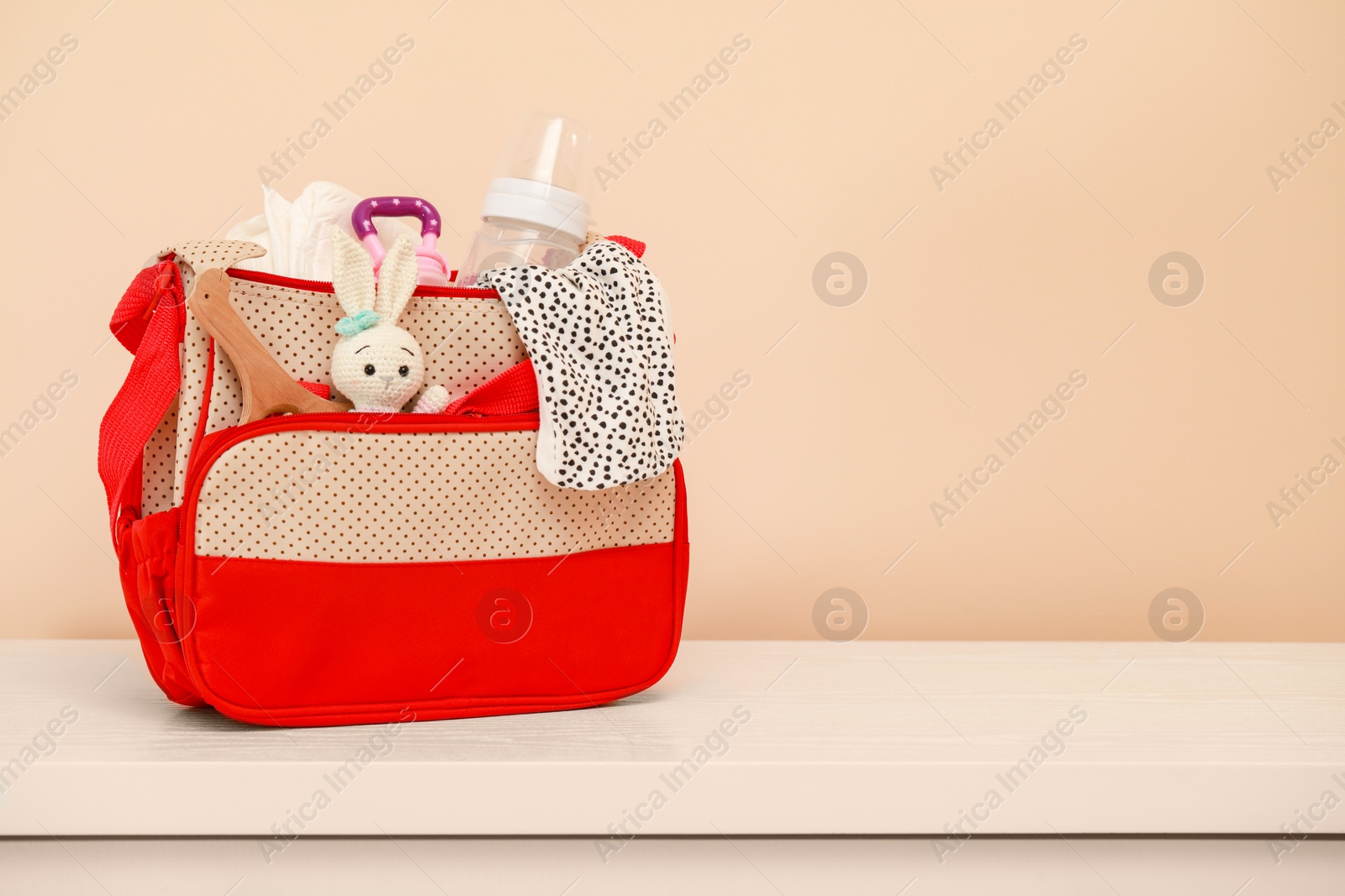 Photo of Mother's bag with baby's stuff on white table near beige wall. Space for text